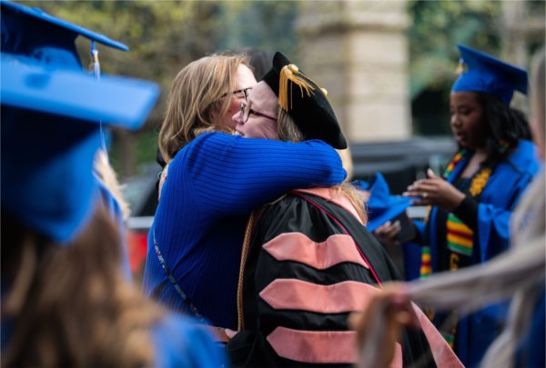  A person hugs a faculty member in regalia before a Commencement ceremony.
