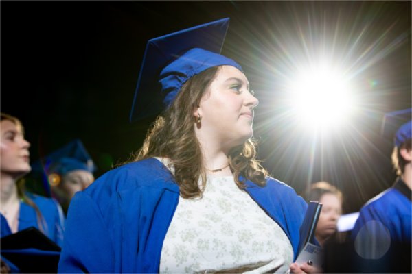  A graduate in blue walks past a beam of light. 