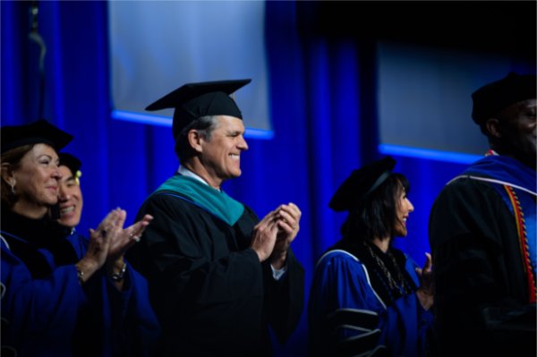  A person wearing regalia claps during a Commencement ceremony. 