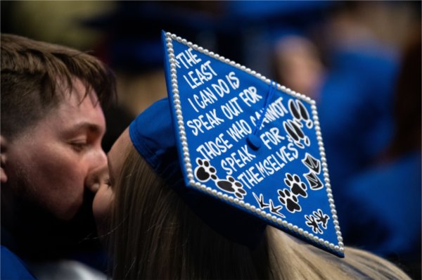 Two graduate kiss while one wears a mortarboard cap. 