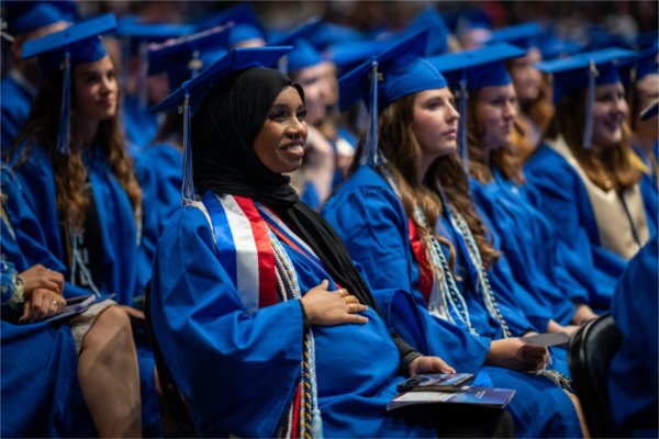  A graduate holds their hand to their belly while wearing a blue cap and gown.