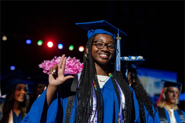  A graduate makes an anchor up hand signal while smiling.