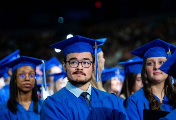 Graduates with their blue caps and gowns listen to a Commencement speaker.
