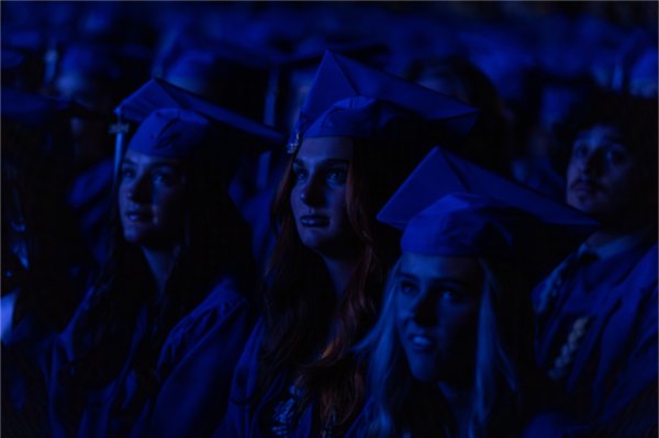  A blue light from a video casts light on the faces of graduates wearing blue caps and gowns. 