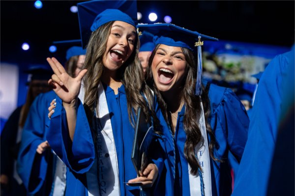   Graduates celebrate as they cross the stage during Commencement with laughs and the anchor up hand sign. 