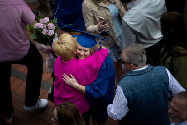  A graduate is hugged by a person while holding pink flowers. 