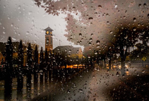  A clock tower is seen through a windshield covered in raindrops.