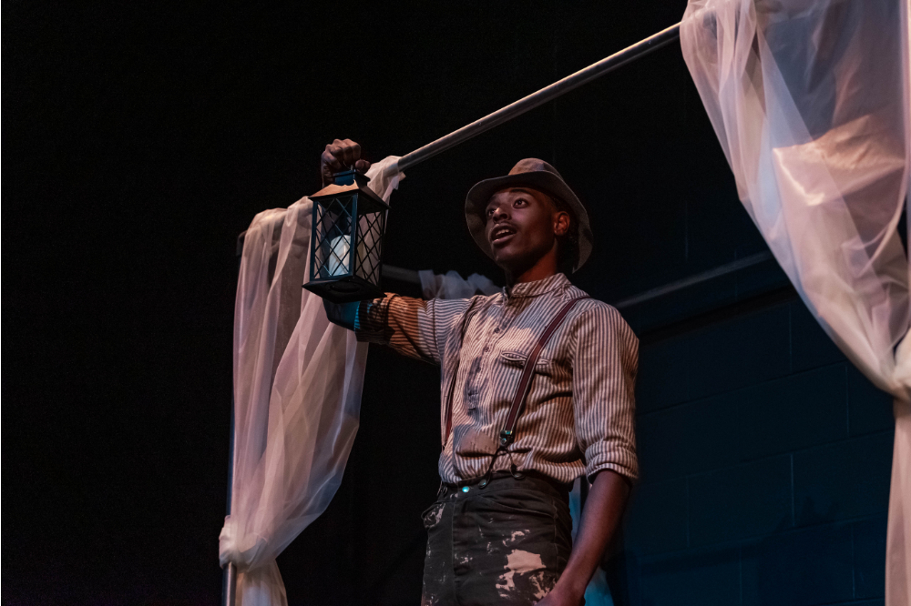 A student actor holding a lantern on stage