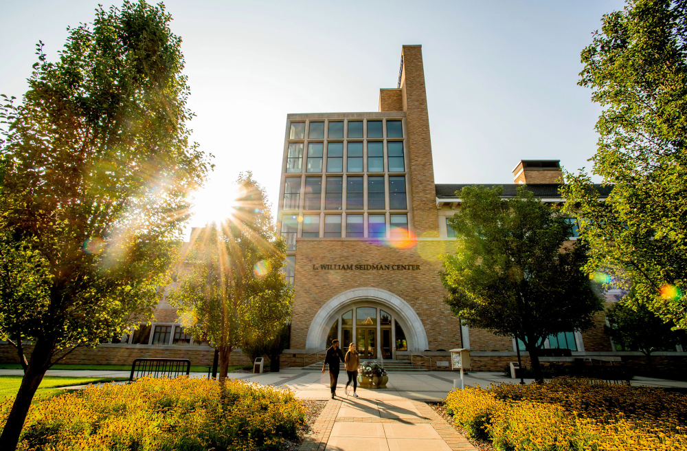 students walking in front of a building with a sun shining through the windows