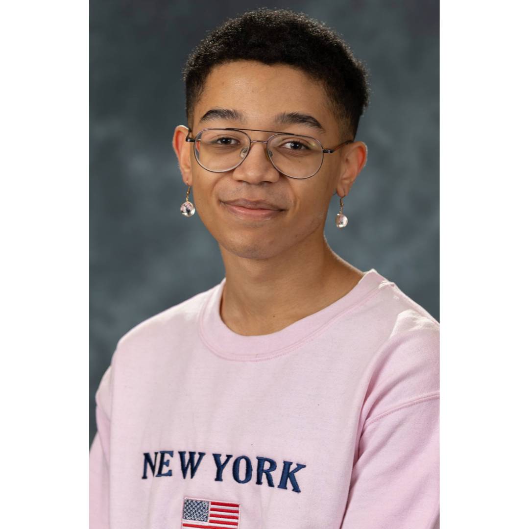 Zuriel wearing glasses and earrings as well as a pink crewneck that says New York and the American flag