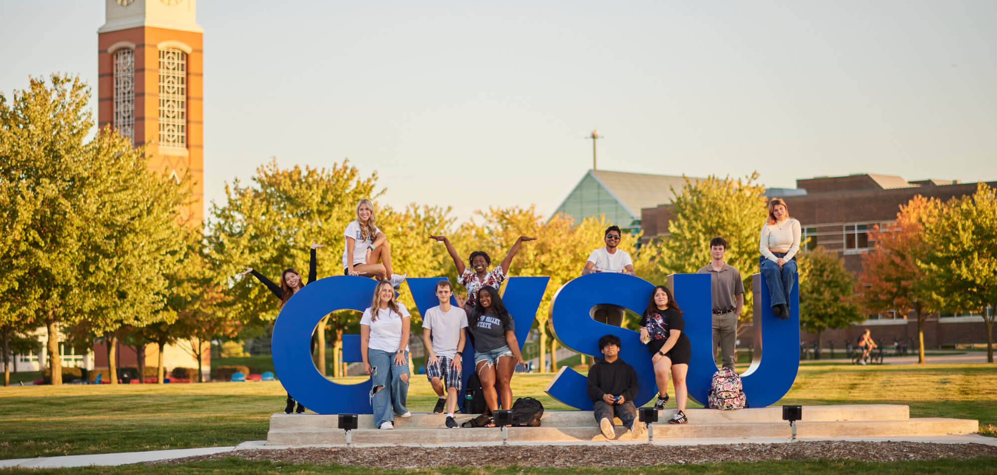 students in front of the GVSU letters structure during golden hour with the clocktower in the background