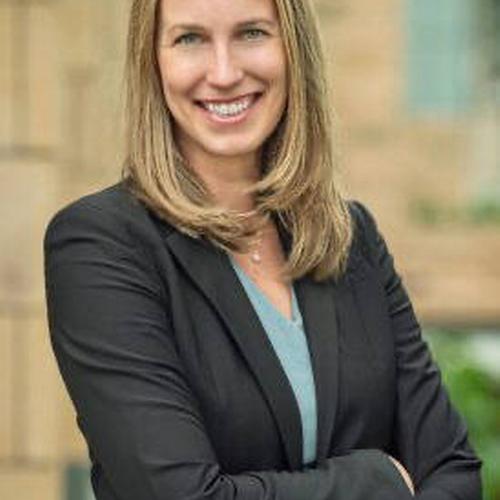 A blonde woman in a blazer smiling at the camera with crossed arms.
