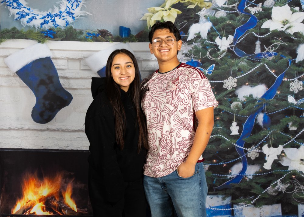two students standing in front of winter themed background with fireplace and christmas tree