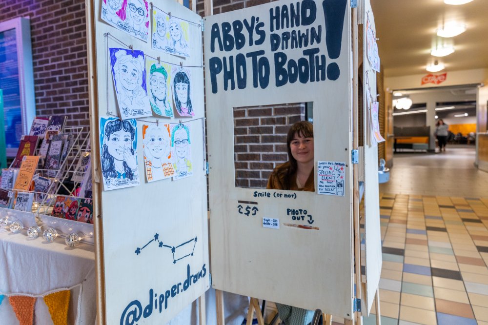 student sitting inside a wooden photobooth
