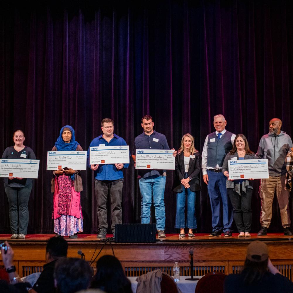 Male and females holding paper checks on stage after the pitch competition