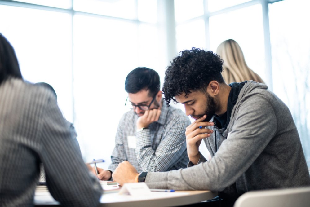 students sit at a desk and write.