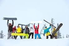 A group of people in ski gear holding up skis and snowboards
