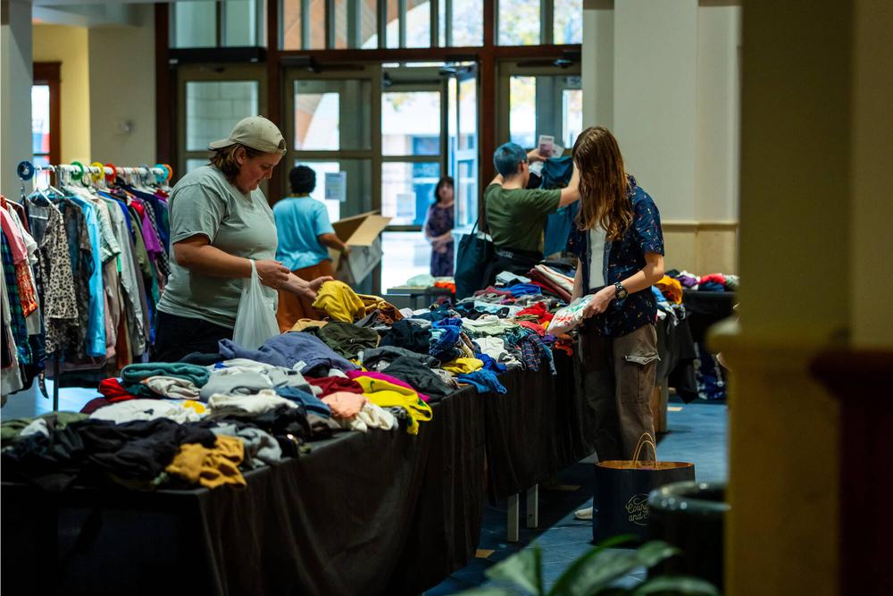 Rows of tables and clothing racks with brightly colored clothes fill the frame, as several attendees peruse the items.
