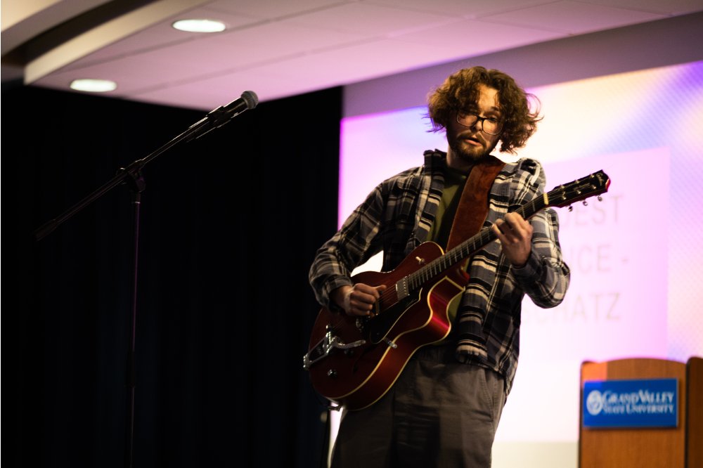 A student standing onstage, playing an electric guitar