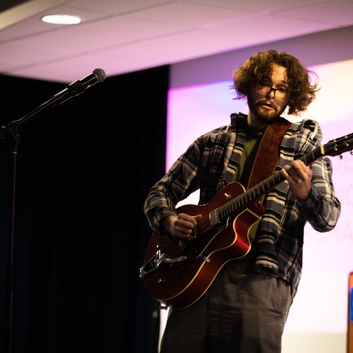 A student standing onstage, playing an electric guitar