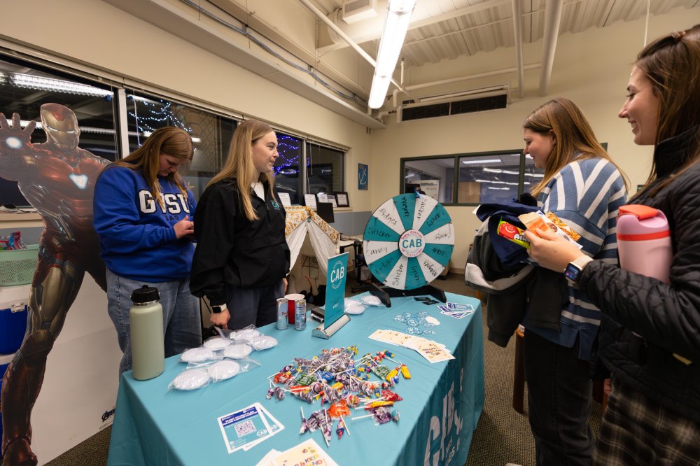 students standing around a table with prizes and a prize wheel