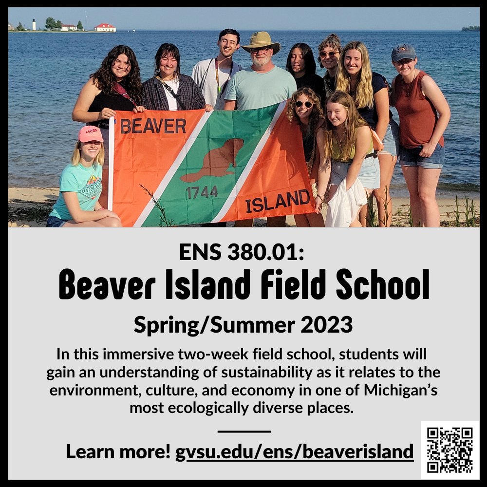 Students and professor standing on the Beaver Island shore, holding a flag, with Lake Michigan in the background