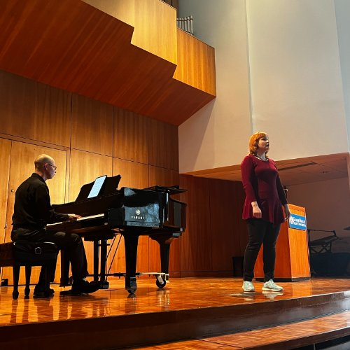 Vocalist singing on stage while accompanied by piano
