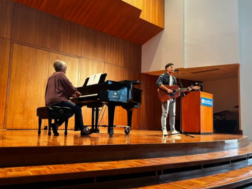 Student playing guitar and singing while accompanied by piano