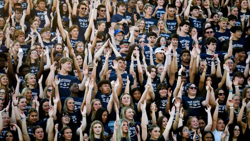 GVSU students at new student orientation with arms raised in a collaborative chant