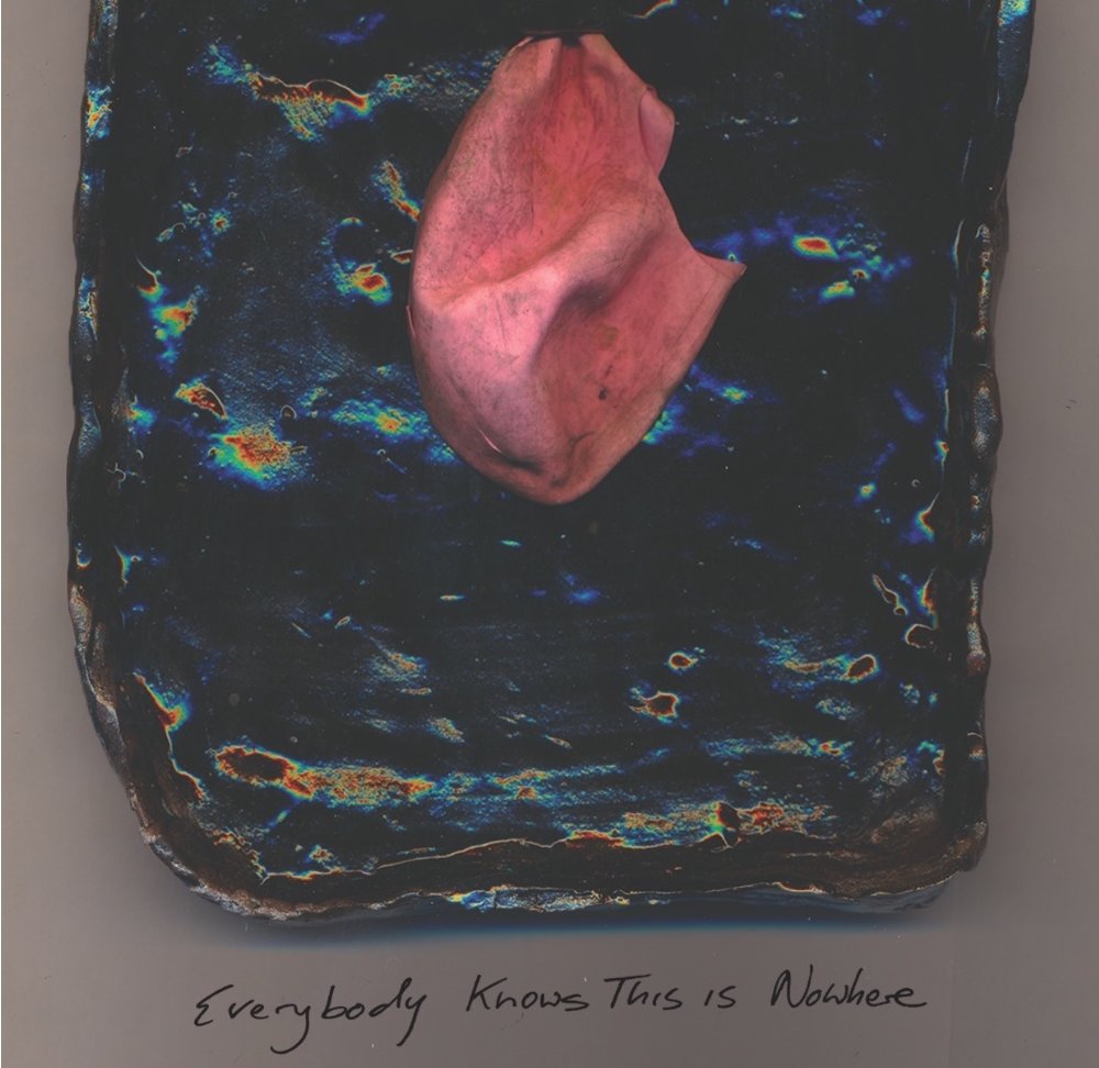 Found pink balloon affixed to black handmade ceramic plaque on wall.