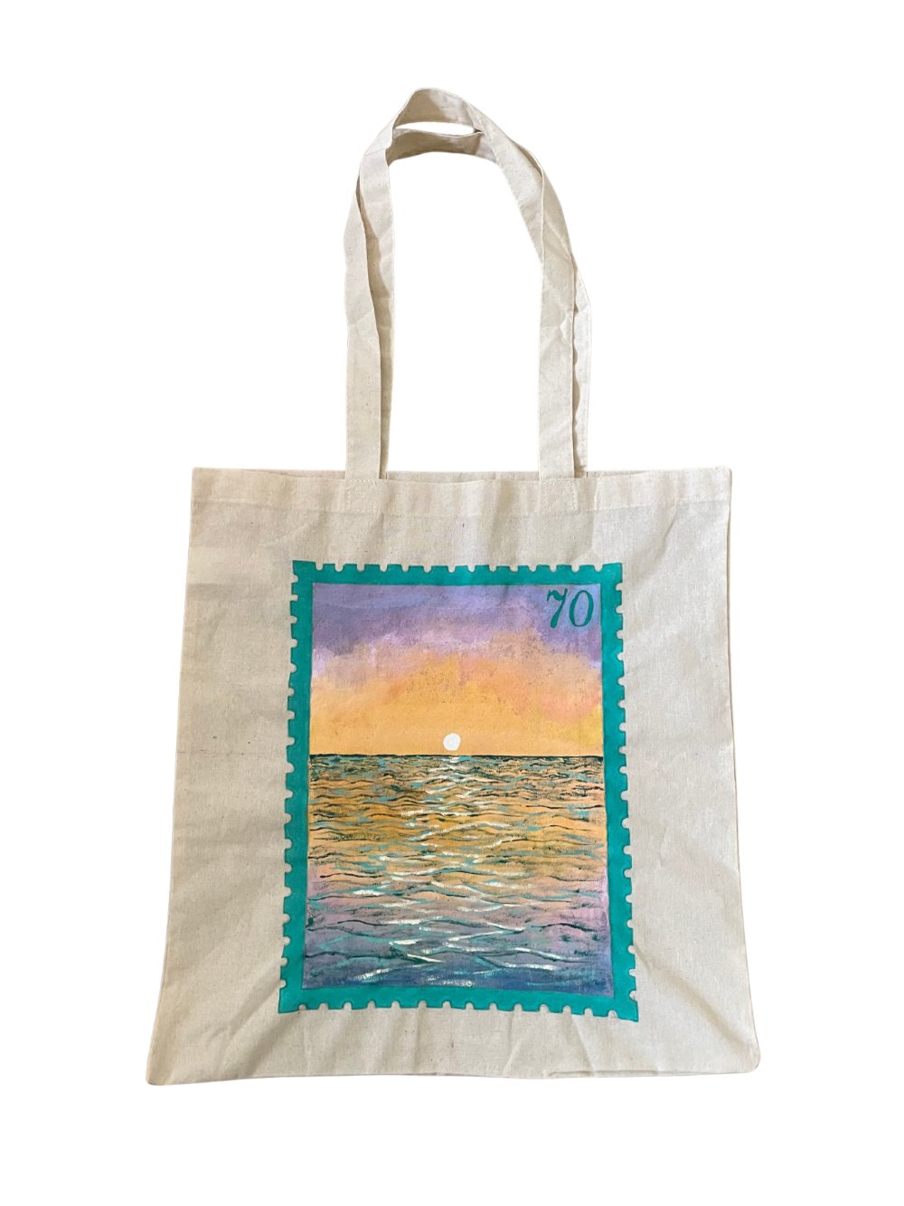 A canvas tote bag that has been painted to feature a stamp edged in teal with a sunset over rippling water. The number 70 is in the top right corner of the stamp.
