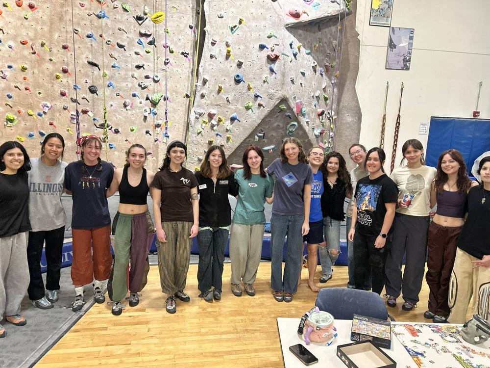 a dozen attendees of the monthly women on the wall program posing for a photo in front of the wall