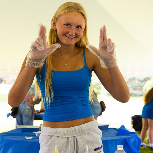 female student making the anchor sign with both hands; wearing a blue tank top and white shorts