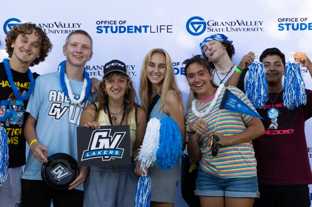 Students wearing GV apparel and posing in front of a GVSU photo backdrop