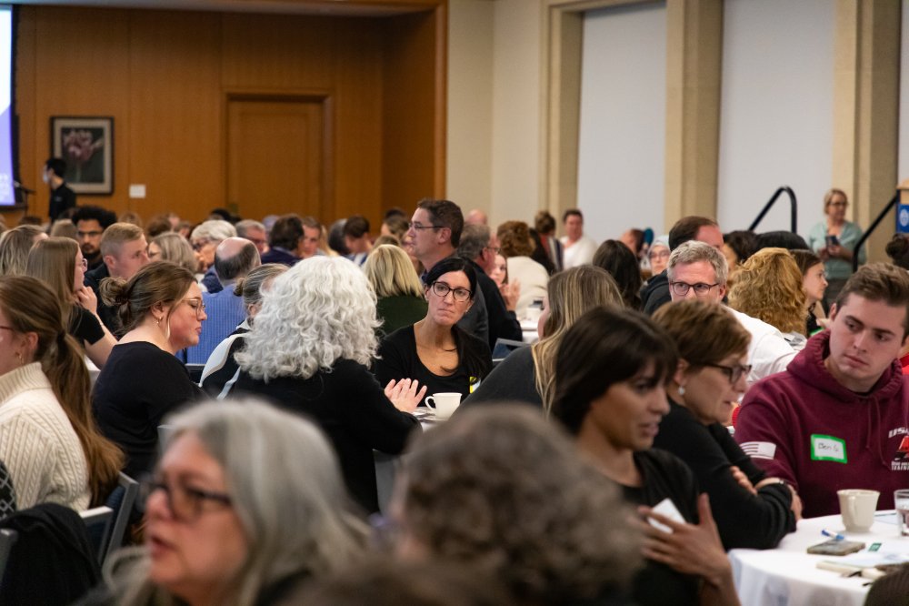 A large group of people seated at round tables engaging in civil discourse