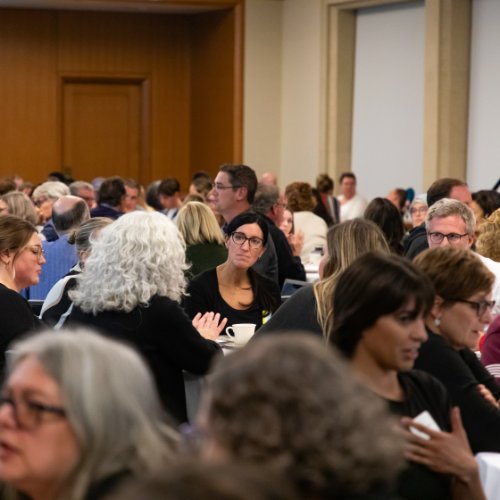 A large group of people seated at round tables engaging in civil discourse
