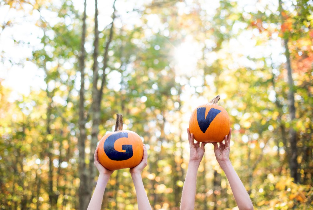 Two pumpkins being lifted into the air, one with a hand painted "G" and the other with a hand painted "V"