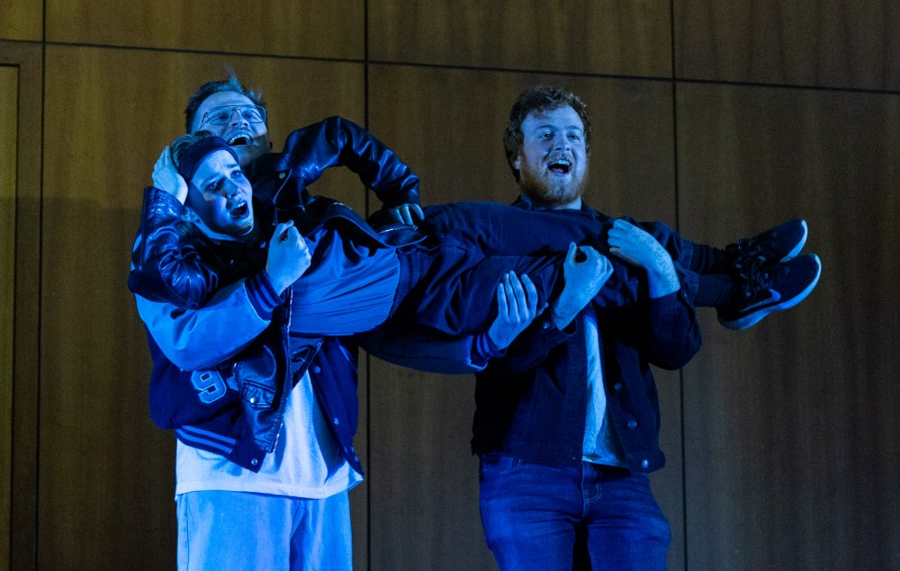 Two students holding up another student while performing on stage