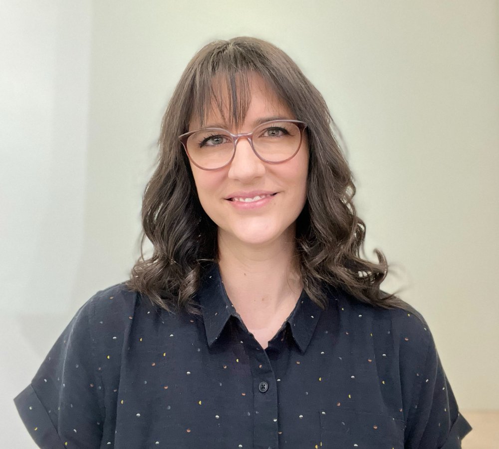 a woman with long dark hair and glasses in a black shirt smiling
