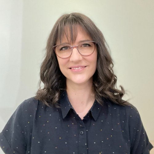 a woman with long dark hair and glasses in a black shirt smiling