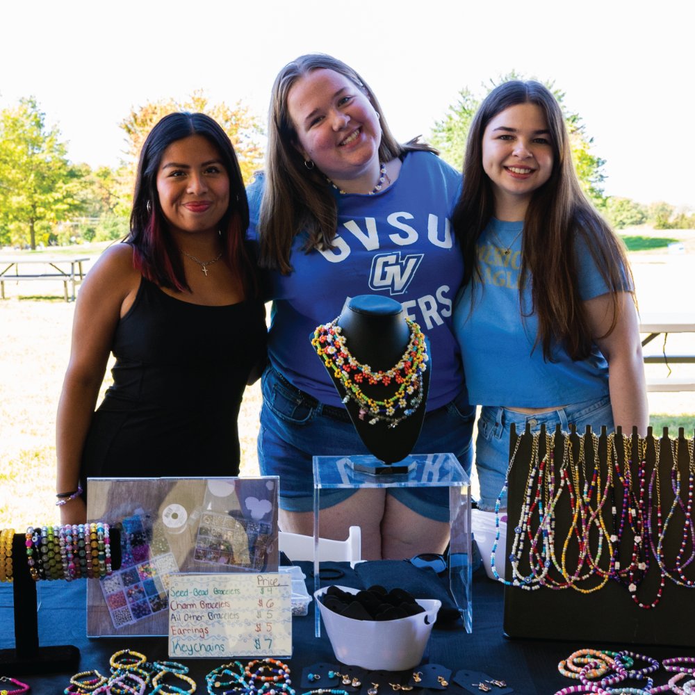 Three women pose over a table displaying jewelry