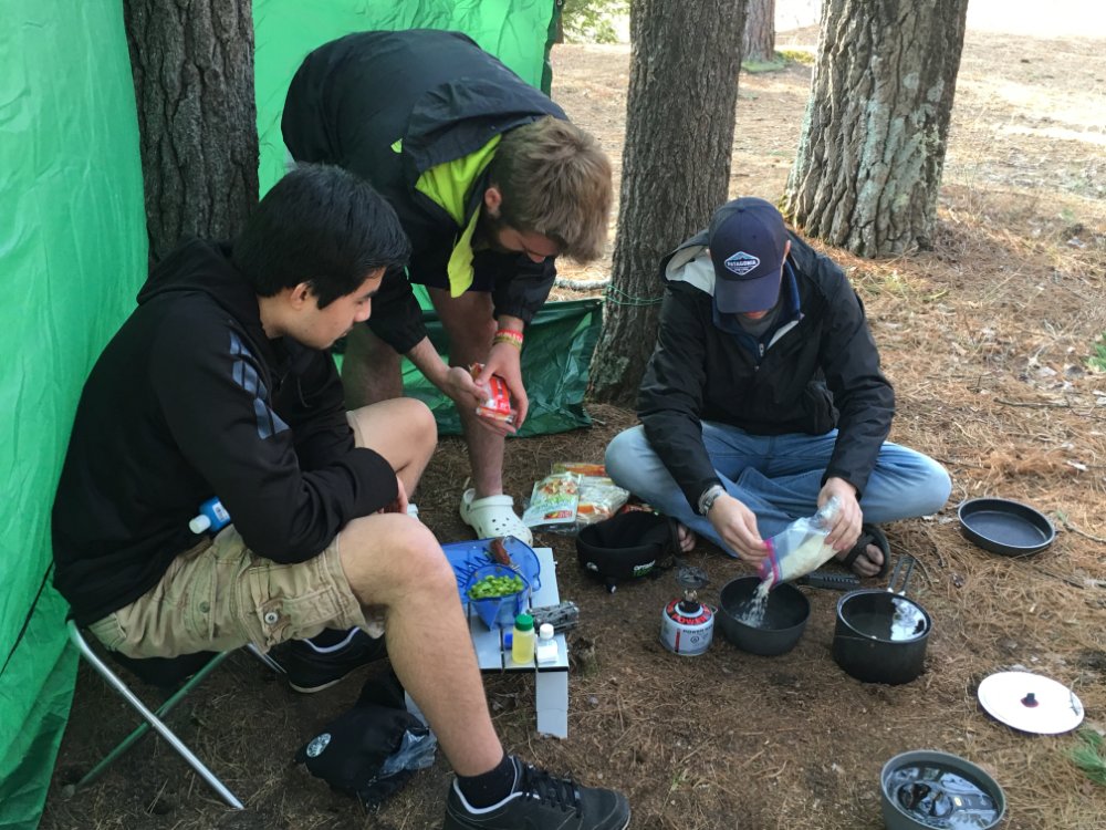 3 students cooking over a hiking stove