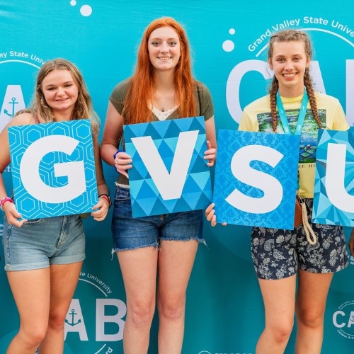 3 girls holding up "GVSU" letters in front of a CAB backdrop