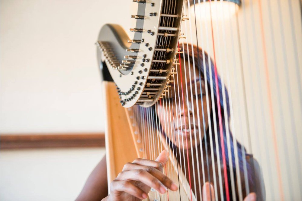 Ahya playing her harp, the camera focus is on her hands and the harp, while her face is slightly blurred behind the harp strings.