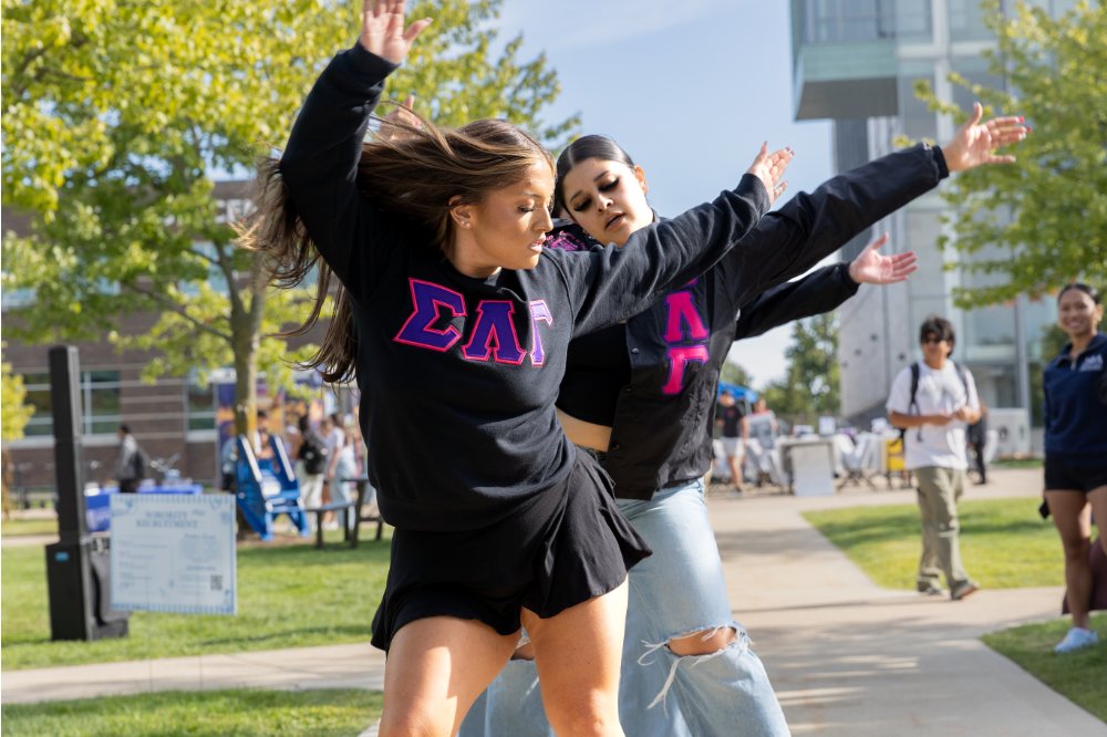 Two students wearing Greek letters and dancing at Meet the Greeks
