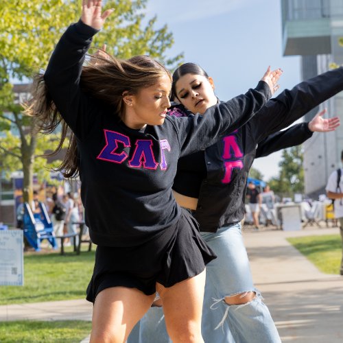 Two students wearing Greek letters and dancing at Meet the Greeks
