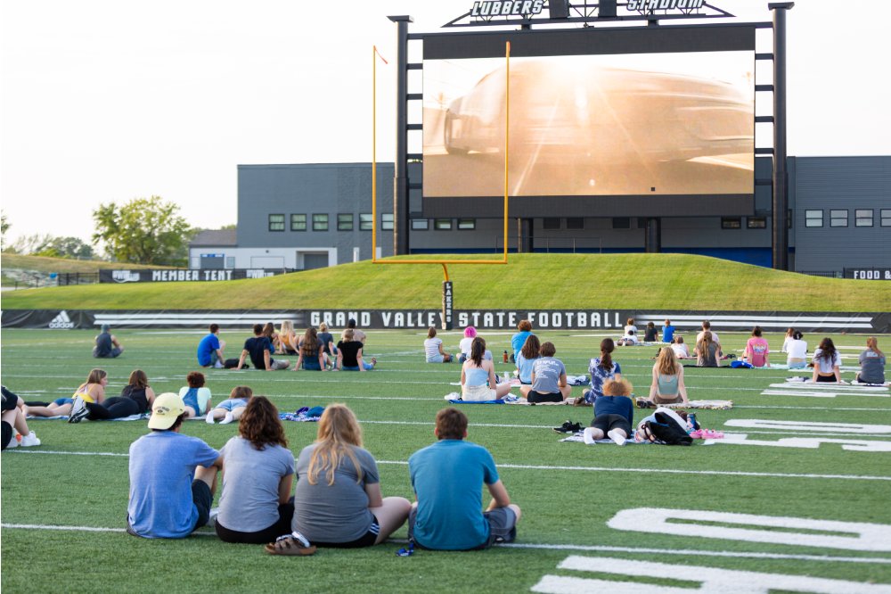Students sitting on the field at Lubbers Stadium, watching a movie on the big screen