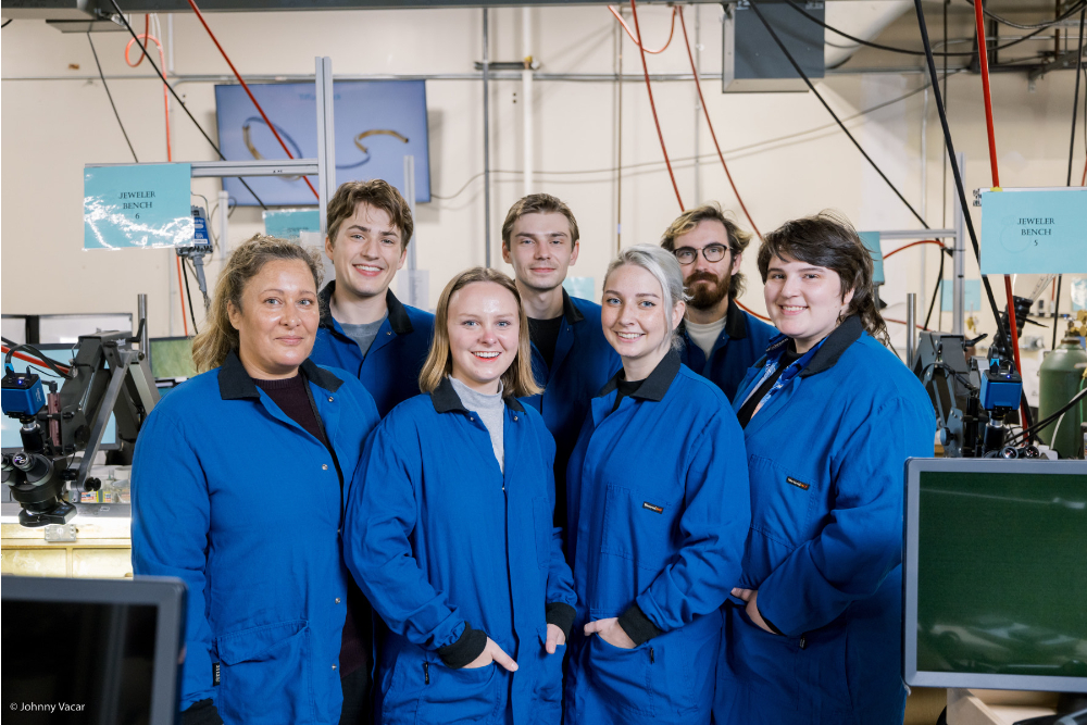 group of seven people standing in blue lab coats in a workshop