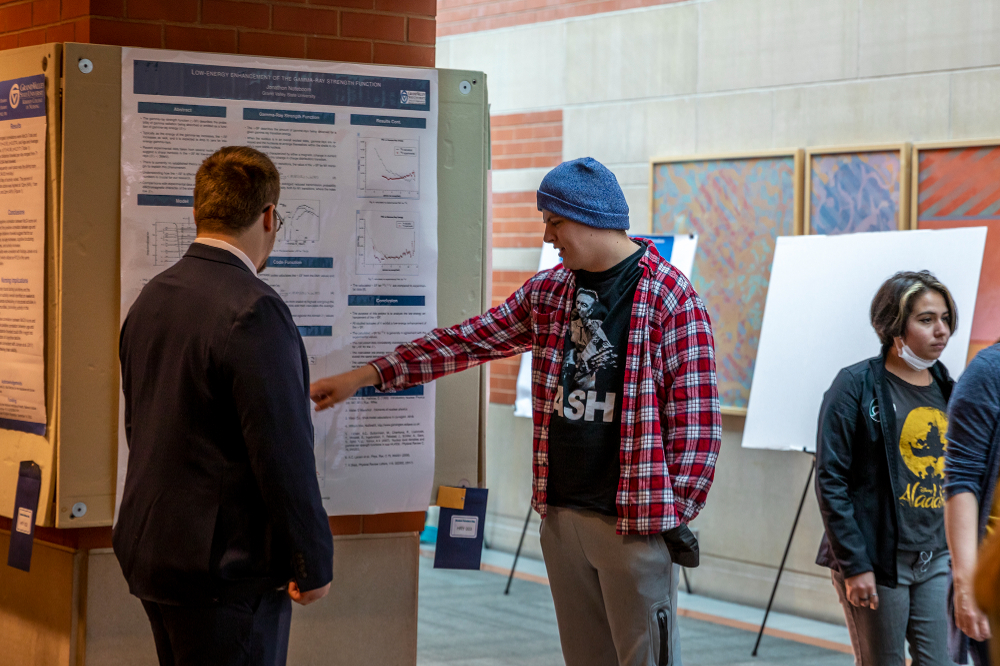 two people standing in front of a poster presentation, person on right is pointing at poster board