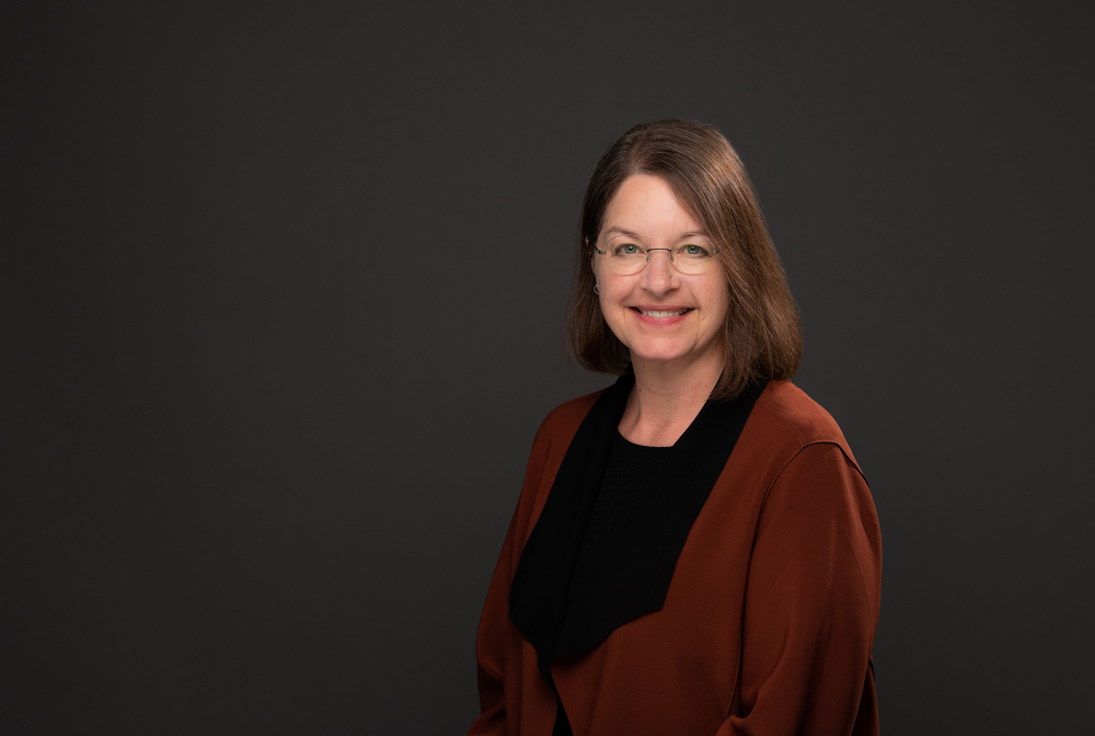 portrait of Christine Rener, wearing a red wrap over a black shirt, she has glasses on